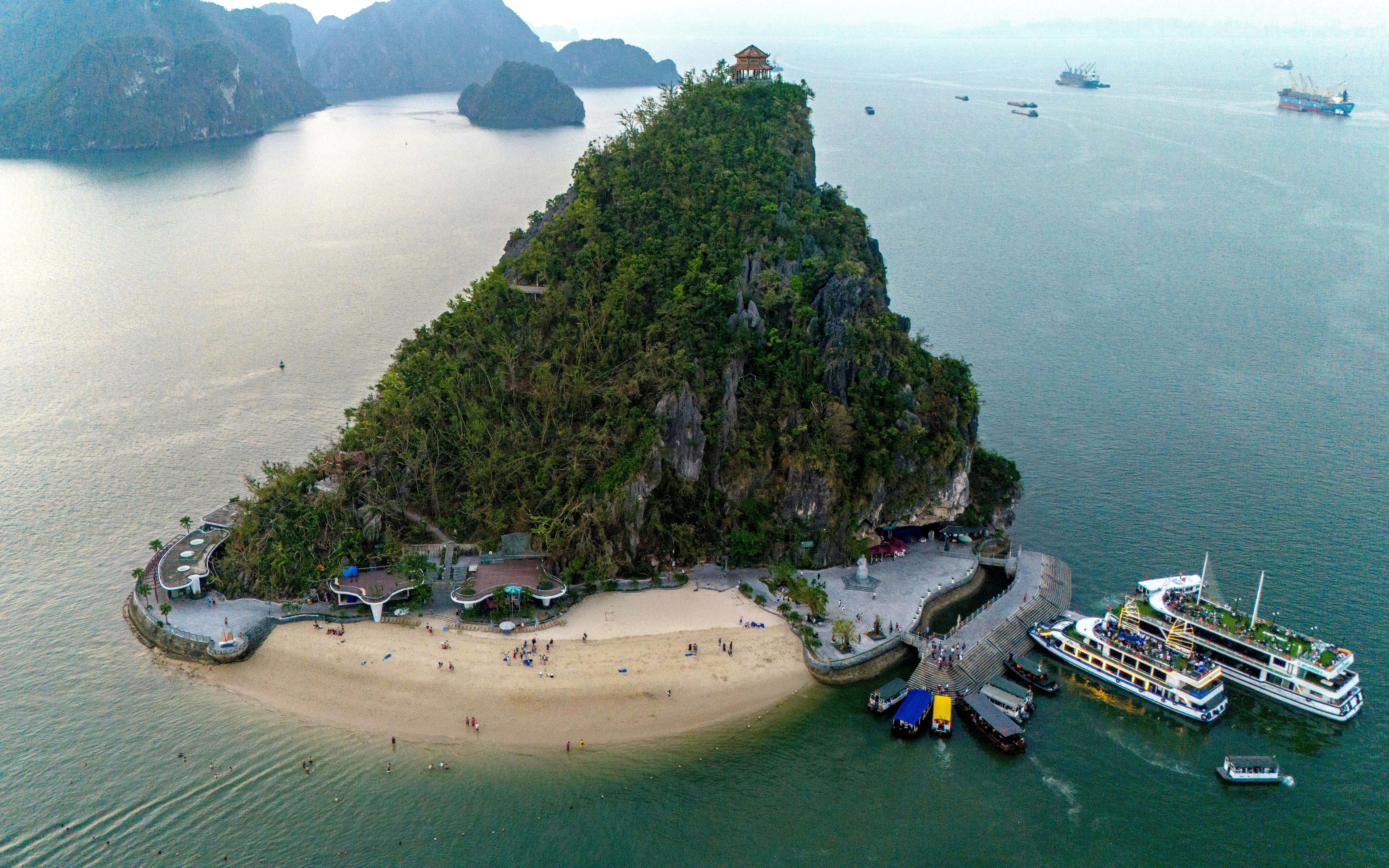 Aerial view of Ti Top Beach Island in Ha Long Bay, Vietnam, with cruise ships at sunset.