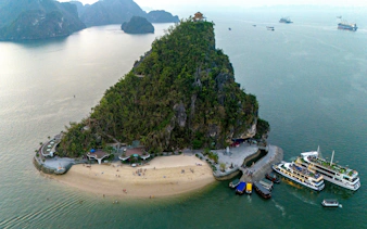 Aerial view of Ti Top Beach Island in Ha Long Bay, Vietnam, with cruise ships at sunset.