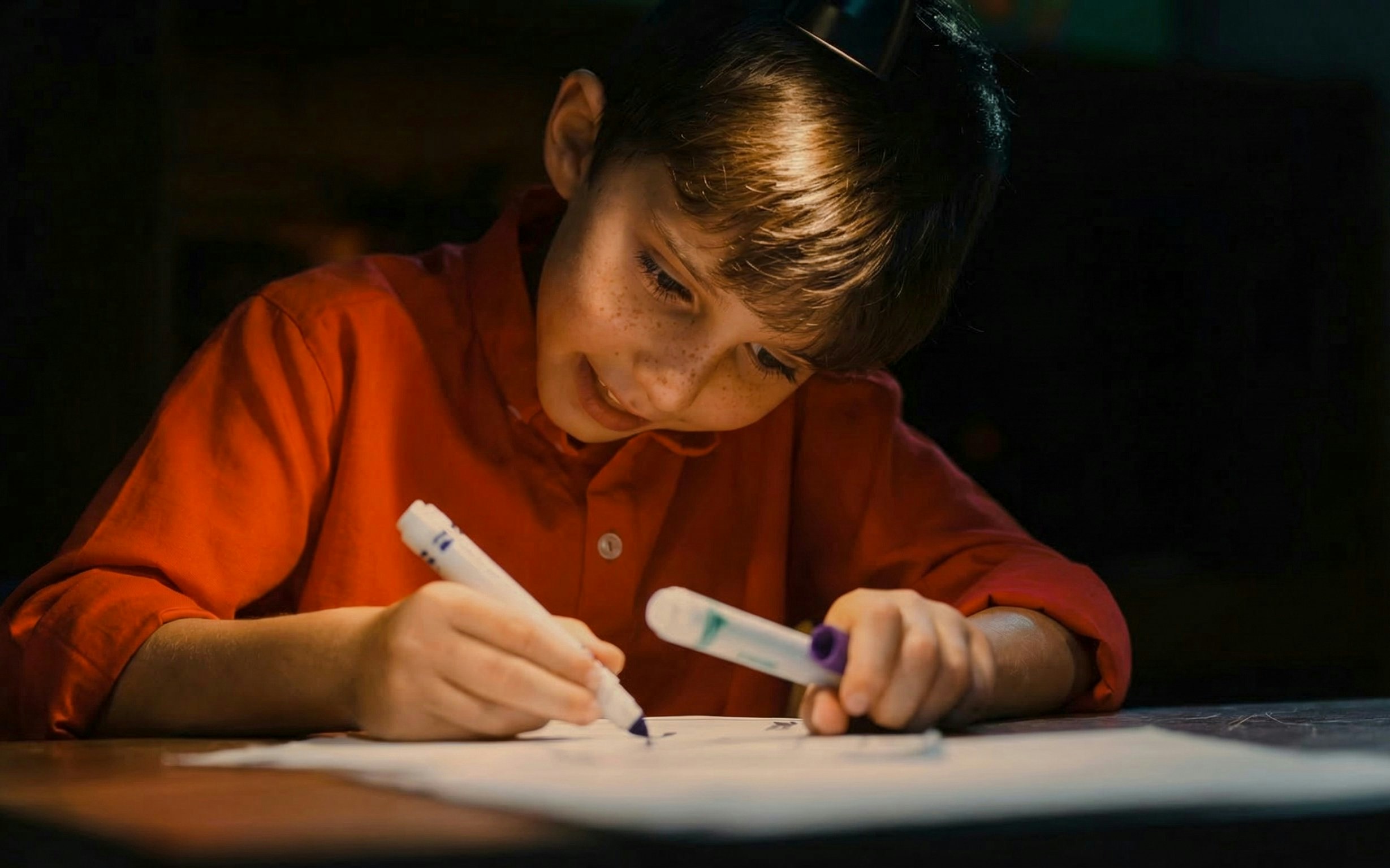 Child drawing with markers, engaged in creative activity.