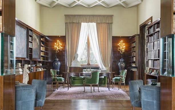 Villa Necchi Campiglio library with green chairs, wooden shelves, and a bust on a desk.