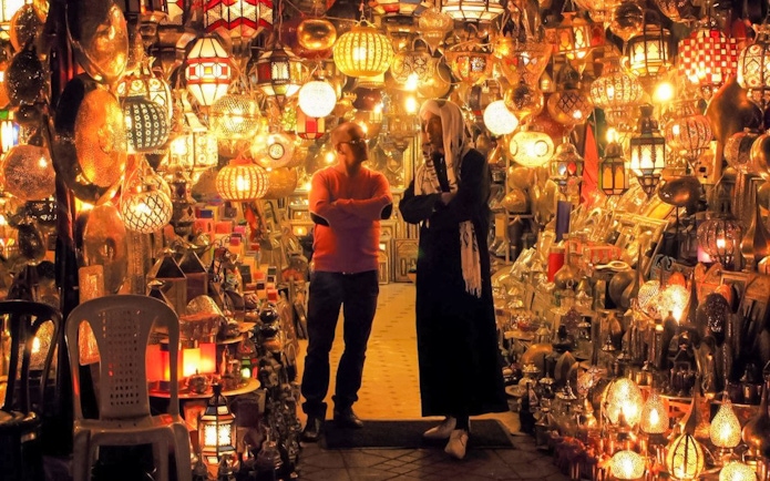 Moroccan market with colorful lanterns and two people conversing, related to vegetable tagine tour.