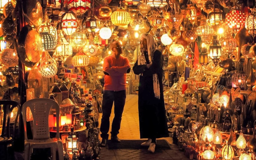 Moroccan market with colorful lanterns and two people conversing, related to vegetable tagine tour.