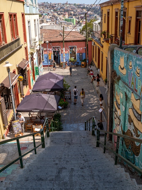 Colorful street art and buildings in Valparaiso, Chile, with people walking down a vibrant alley.