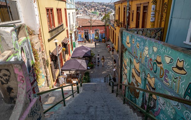 Colorful street art and buildings in Valparaiso, Chile, with people walking down a vibrant alley.