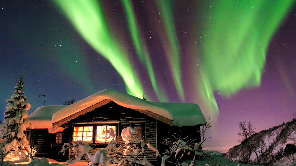 Northern Lights over snowy cabin at Chena Hot Springs, Alaska.