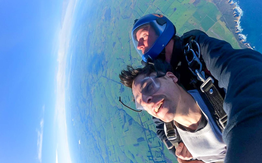 Tandem skydiver smiling above fields and coastline near the 12 Apostles, Victoria.