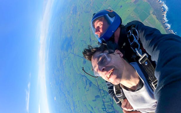 Tandem skydiver smiling above fields and coastline near the 12 Apostles, Victoria.