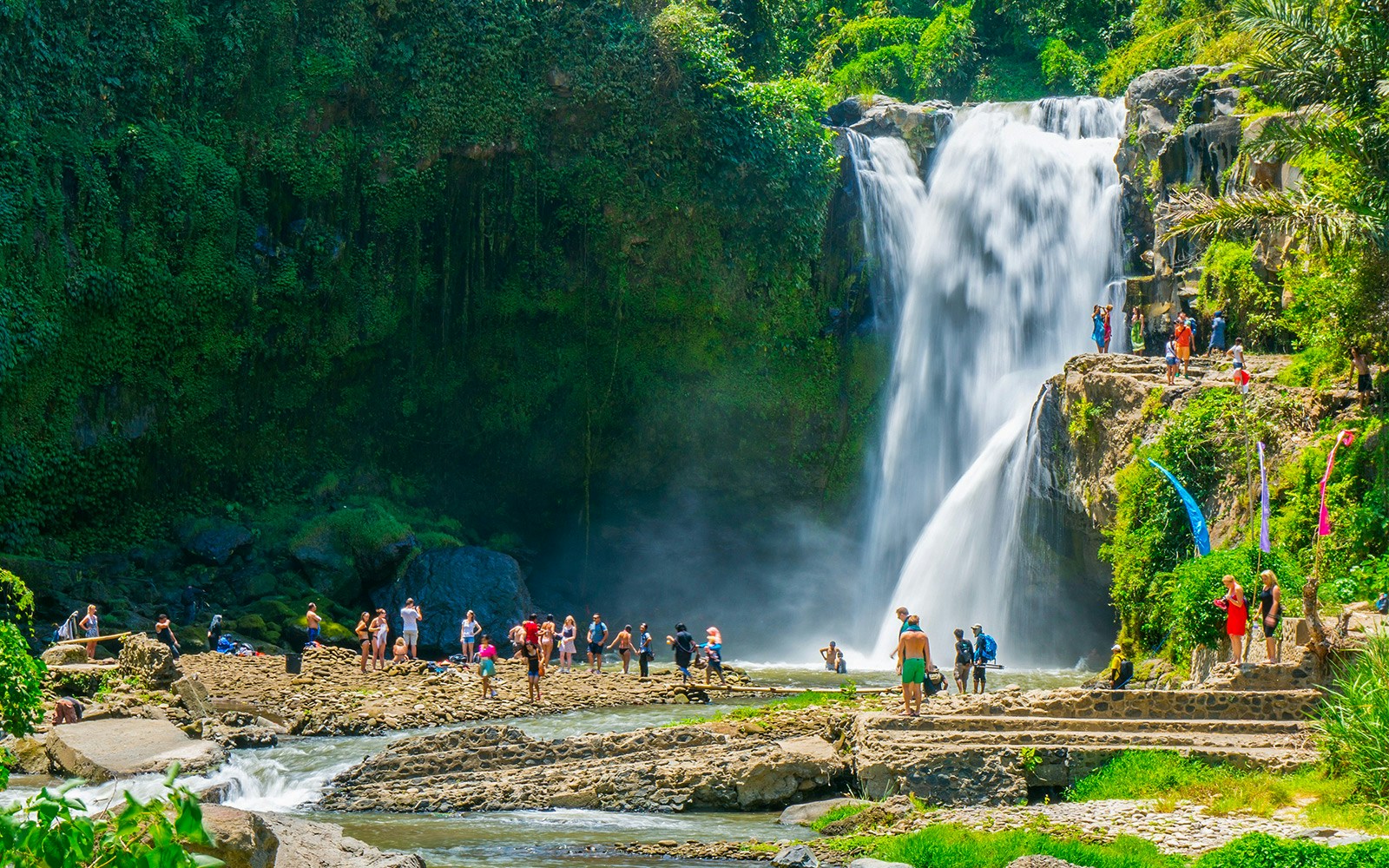 Tourists exploring Tegenungan Waterfall surrounded by lush greenery in Ubud, Bali.