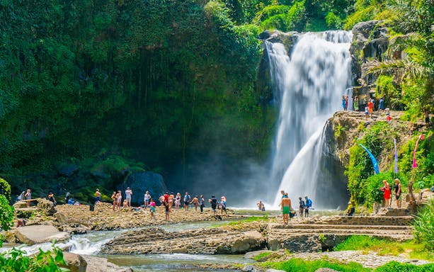 Tourists exploring Tegenungan Waterfall surrounded by lush greenery in Ubud, Bali.