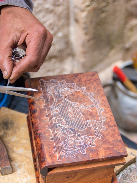 Artist crafting intricate design on wooden box at artisan shop in Chefchaouen.