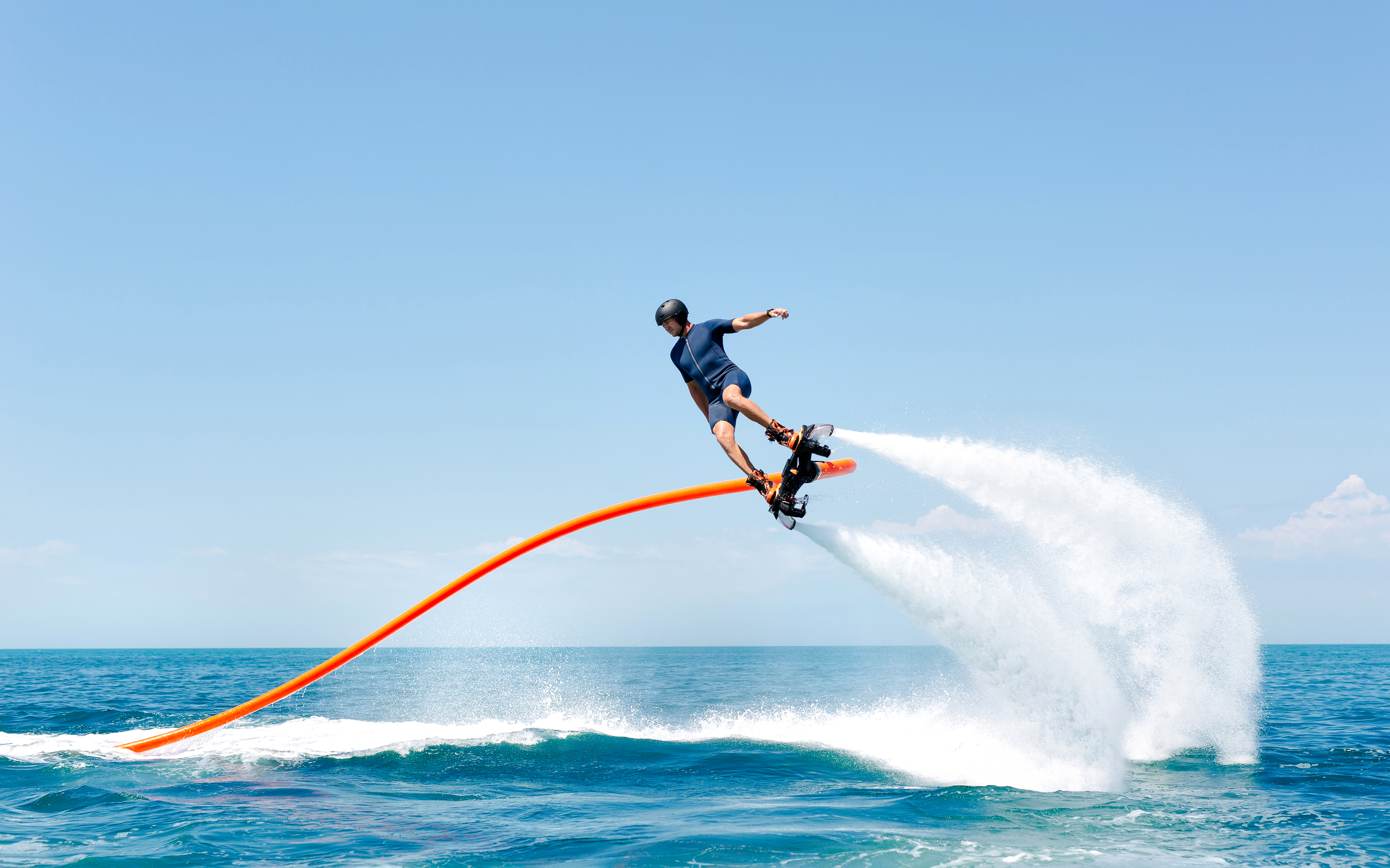 Man performing tricks on a flyboard over the ocean.