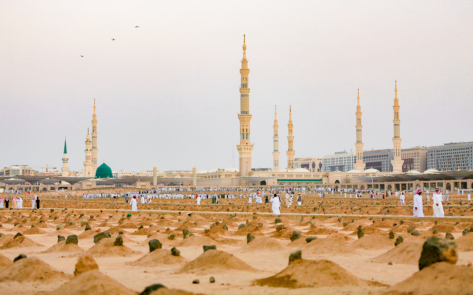Pilgrims at Al-Masjid an-Nabawi with its iconic green dome and minarets in Medina, Saudi Arabia.