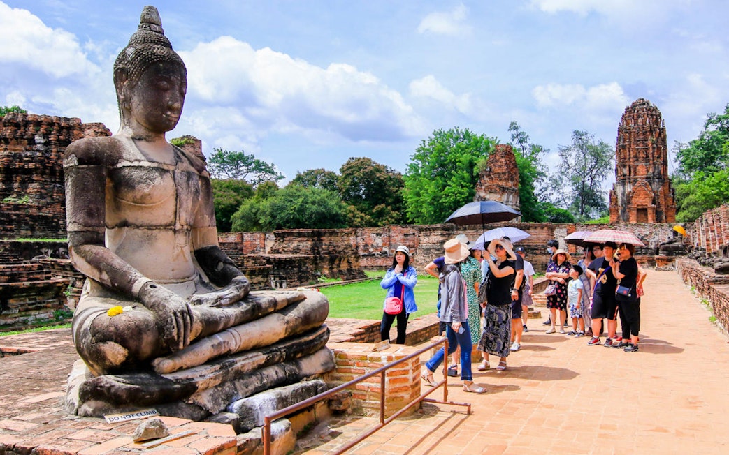 Tourists exploring ancient Buddha statue at Ayutthaya Historical Park, Thailand.