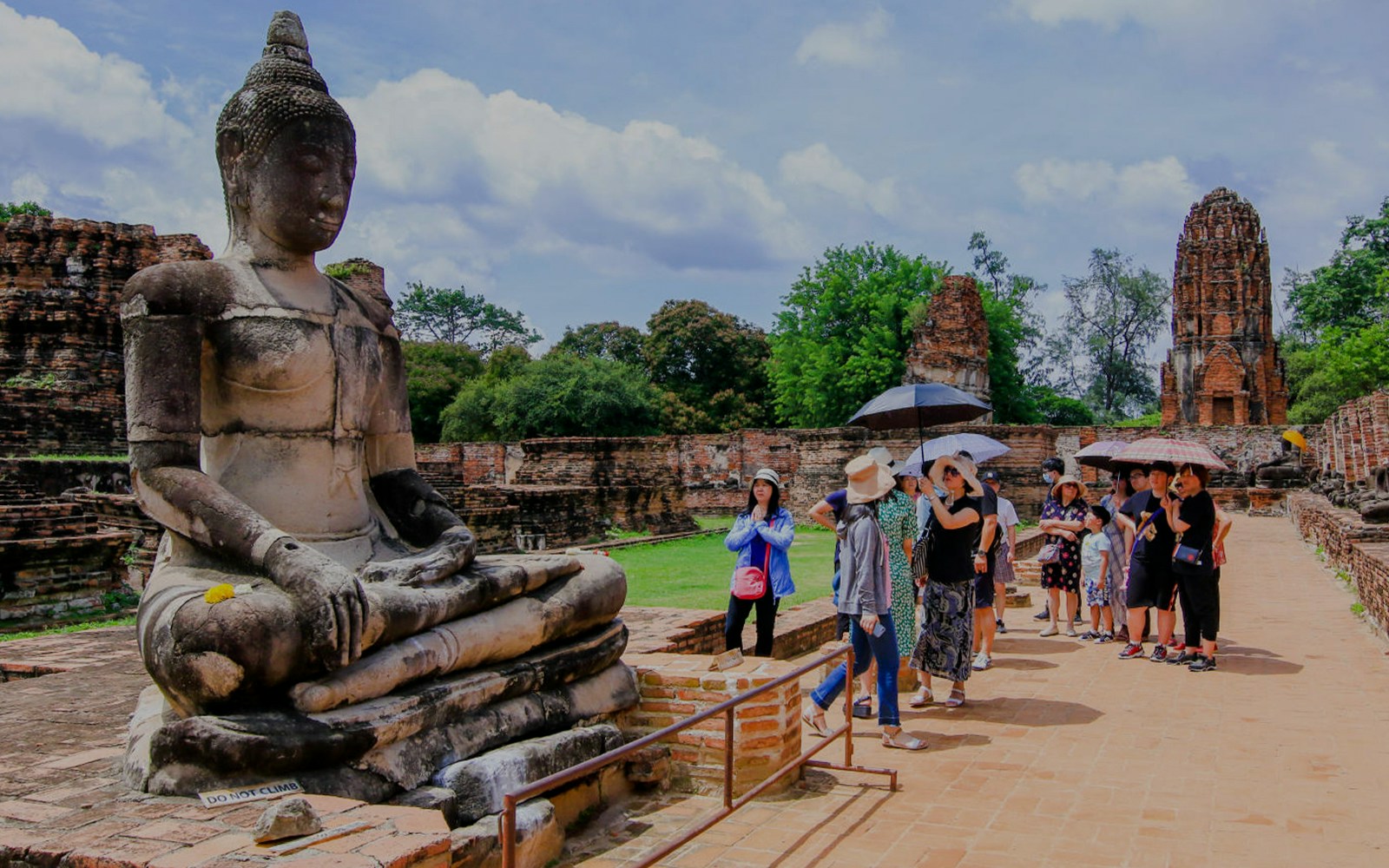 Tourists exploring ancient Buddha statue at Ayutthaya Historical Park, Thailand.