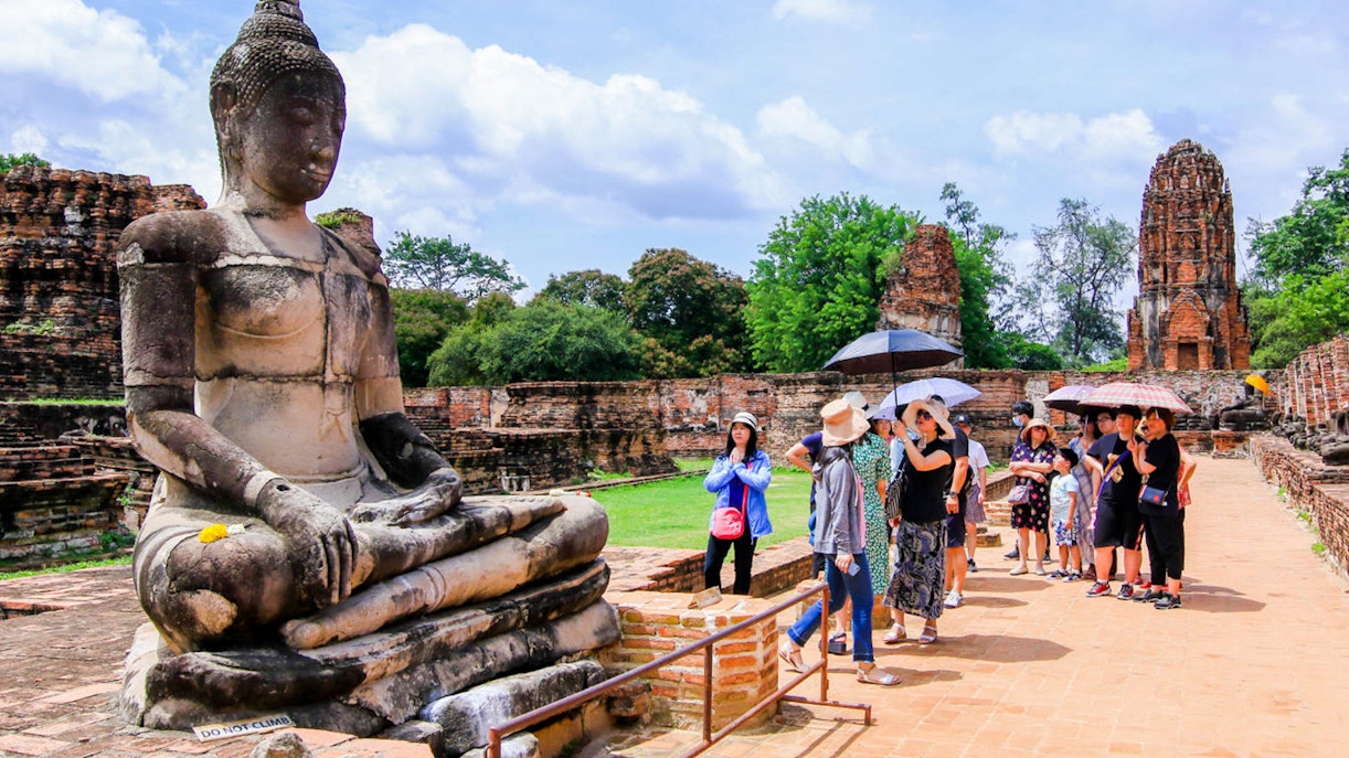 Tourists exploring ancient Buddha statue at Ayutthaya Historical Park, Thailand.
