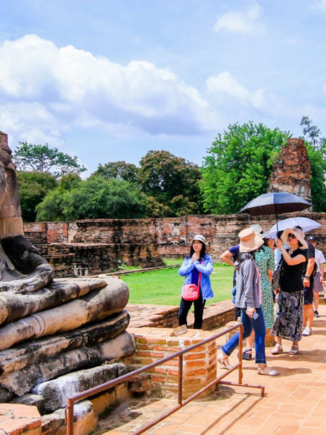 Tourists exploring ancient Buddha statue at Ayutthaya Historical Park, Thailand.