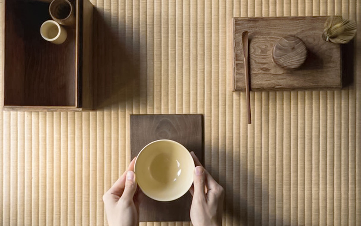 Hands holding a bowl on a tatami mat during a Tokyo matcha tea ceremony.