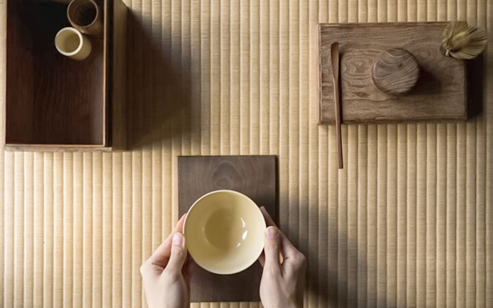 Hands holding a bowl on a tatami mat during a Tokyo matcha tea ceremony.