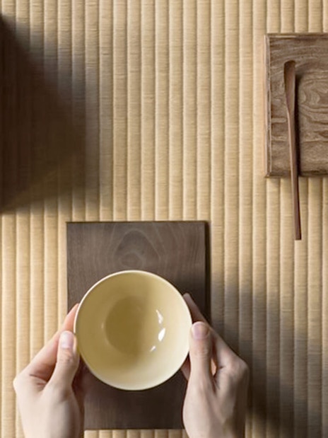 Hands holding a bowl on a tatami mat during a Tokyo matcha tea ceremony.