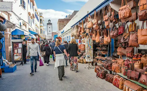Essaouira Medina market street with leather bags and tourists, Marrakesh day trip.