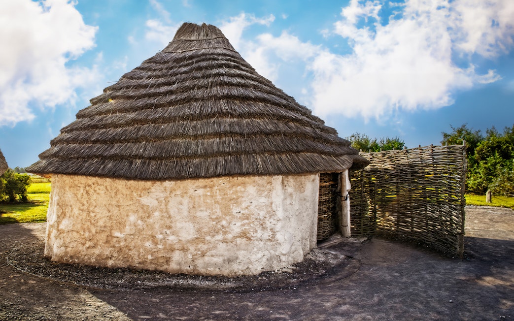 Recreation of ancient Stonehenge builder's house with thatched roof and wattle fence.