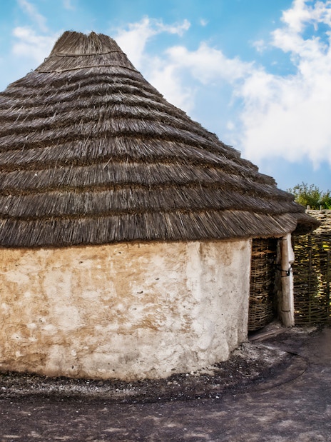 Recreation of ancient Stonehenge builder's house with thatched roof and wattle fence.
