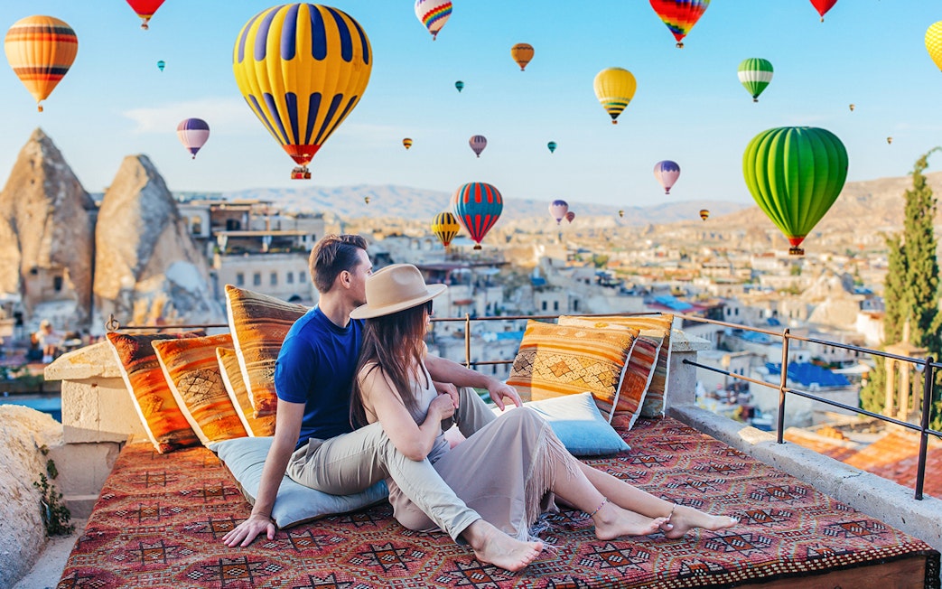 Couple relaxing on terrace watching hot air balloons in Cappadocia, Turkey.