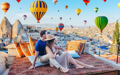 Couple relaxing on terrace watching hot air balloons in Cappadocia, Turkey.
