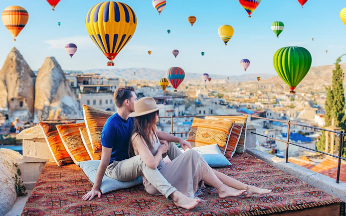 Couple relaxing on terrace watching hot air balloons in Cappadocia, Turkey.