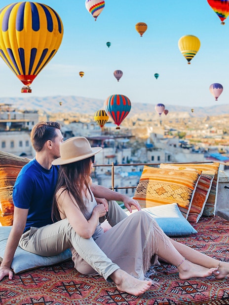 Couple relaxing on terrace watching hot air balloons in Cappadocia, Turkey.