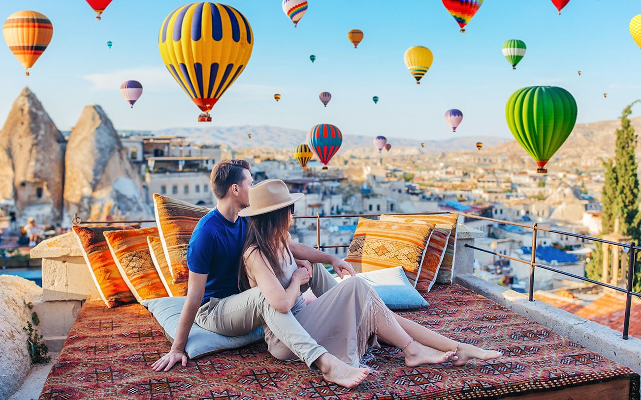 Couple relaxing on terrace watching hot air balloons in Cappadocia, Turkey.