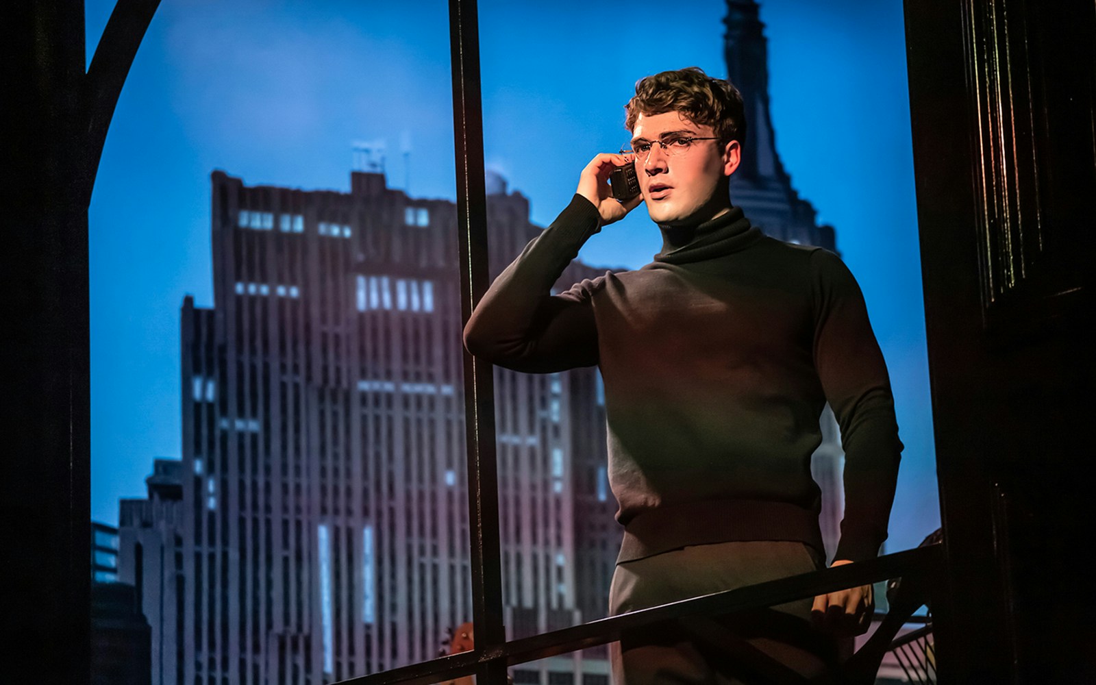 Actor on stage during "Cruel Intentions: The 90's Musical" with cityscape backdrop.