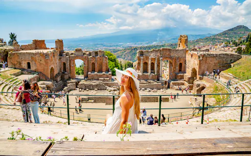 Tourist enjoying view at Taormina Ancient Theatre, Sicily, with ruins and landscape in background.