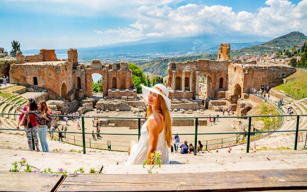 Tourist enjoying view at Taormina Ancient Theatre, Sicily, with ruins and landscape in background.
