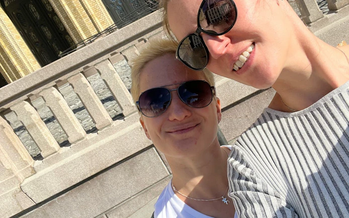 Two people smiling in front of a historic building in Oslo during a self-guided city exploration game.