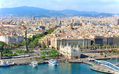 Aerial view of Barcelona's waterfront and cityscape, featuring Montjuic in the background.