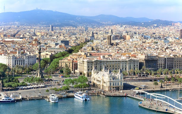 Aerial view of Barcelona's waterfront and cityscape, featuring Montjuic in the background.