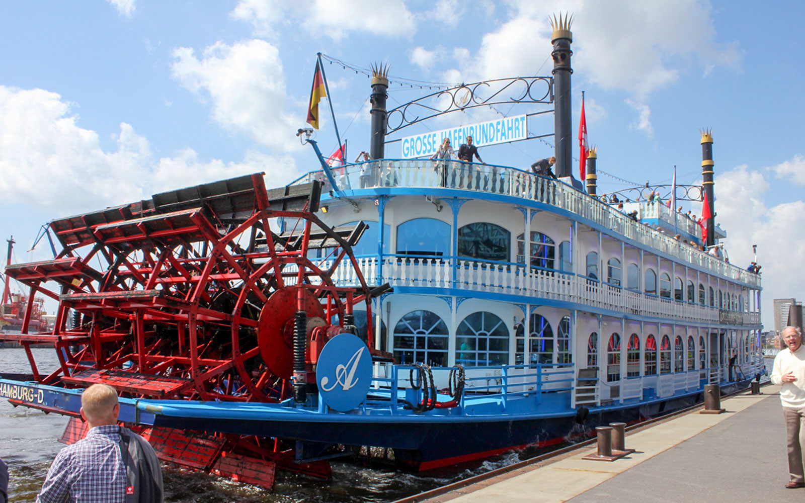 Paddle steamer docked in Hamburg, Germany, with passengers on deck.