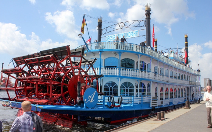 Paddle steamer docked in Hamburg, Germany, with passengers on deck.