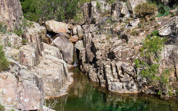 Trekker crossing rocky terrain towards Piscina Irgas Waterfall in Villacidro, Sardinia.