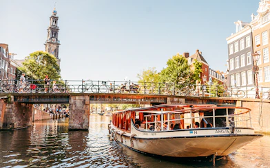 Canal boat under bridge in Amsterdam with Westerkerk tower in background.