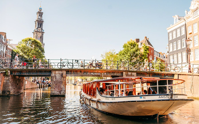 Canal boat under bridge in Amsterdam with Westerkerk tower in background.