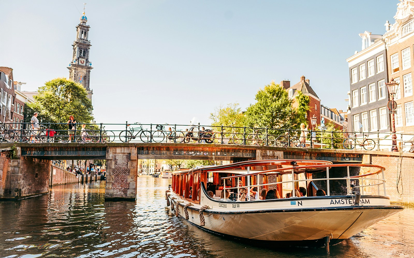 Canal boat under bridge in Amsterdam with Westerkerk tower in background.