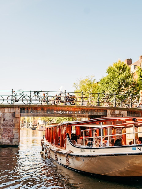 Canal boat under bridge in Amsterdam with Westerkerk tower in background.