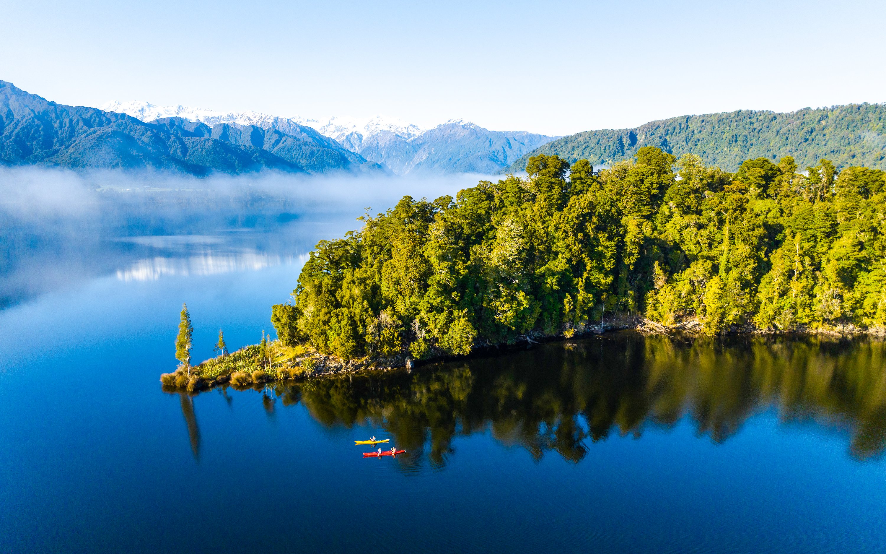 Visitors kayaking on Lake Mapourika with lush forest and mountains in the background.