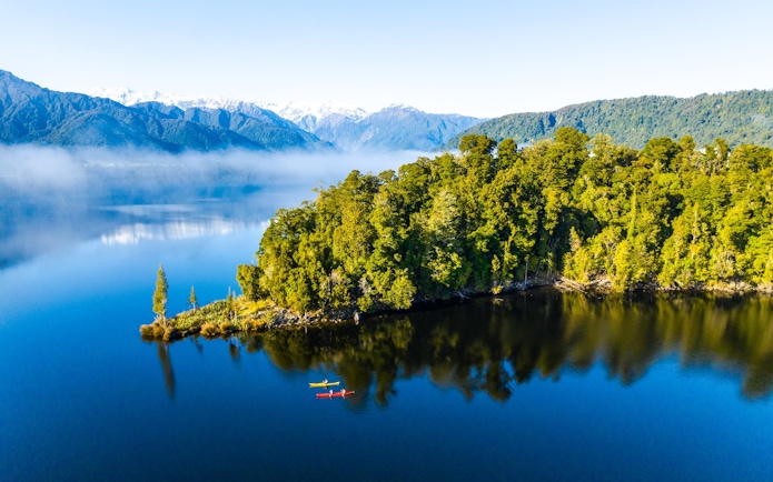 Visitors kayaking on Lake Mapourika with lush forest and mountains in the background.