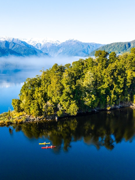 Visitors kayaking on Lake Mapourika with lush forest and mountains in the background.