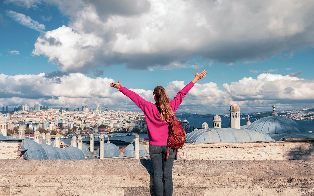 Person overlooking Istanbul skyline near Galata Tower, arms raised in excitement.