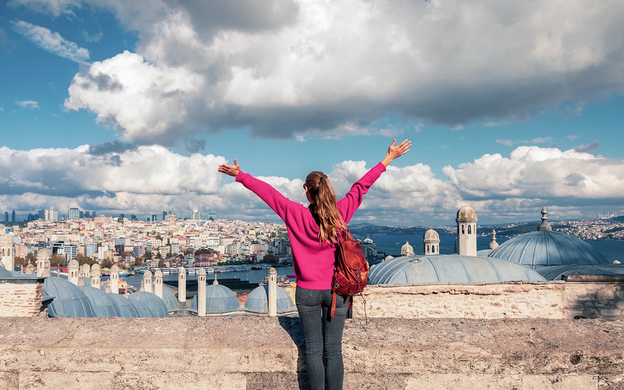 Person overlooking Istanbul skyline near Galata Tower, arms raised in excitement.