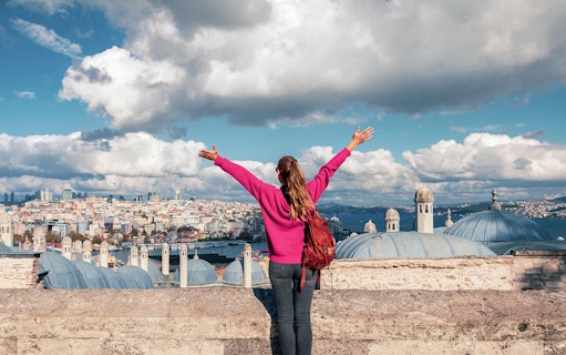 Person overlooking Istanbul skyline near Galata Tower, arms raised in excitement.